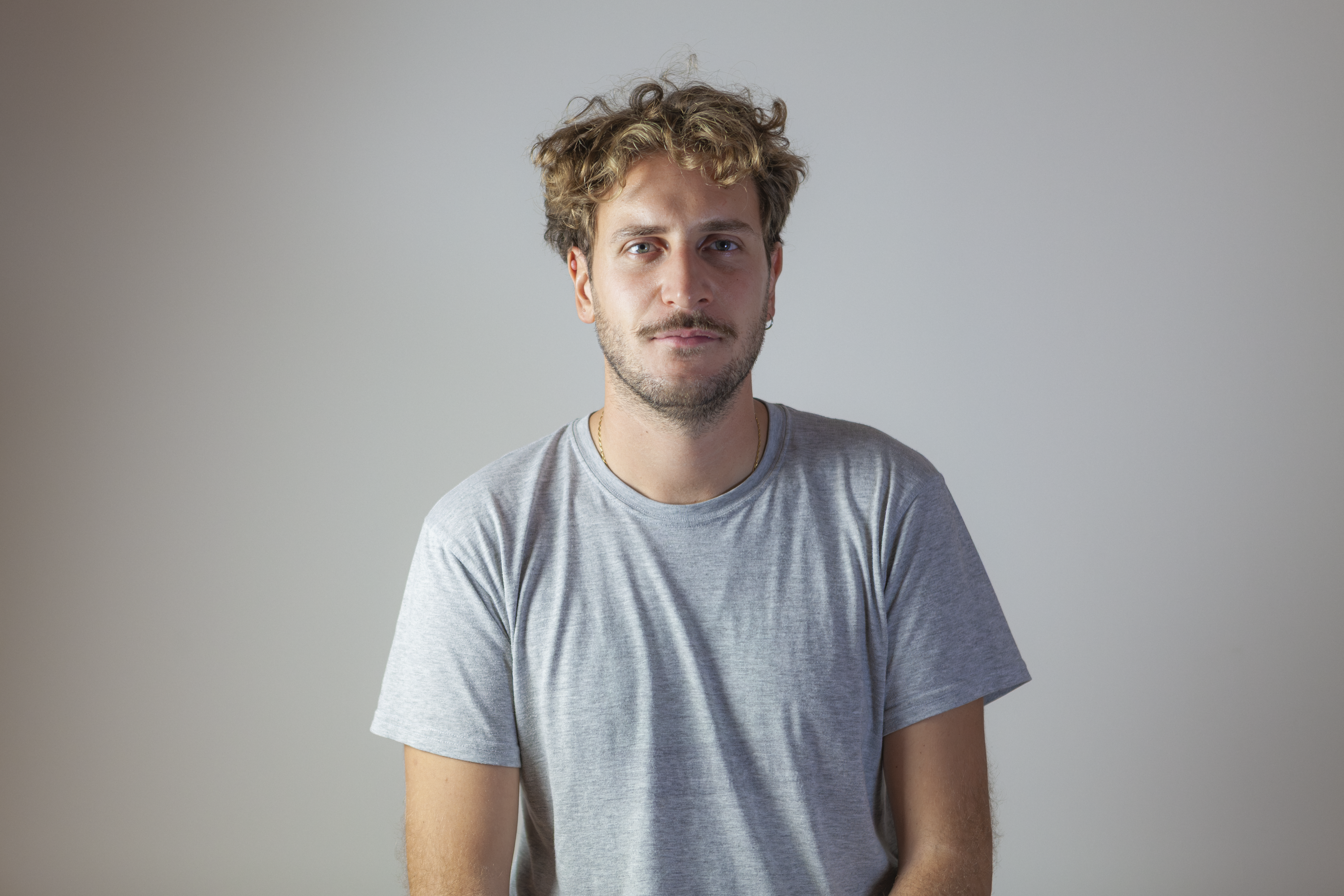 Portrait of a man with brown hair and glasses on a flat gray background.
